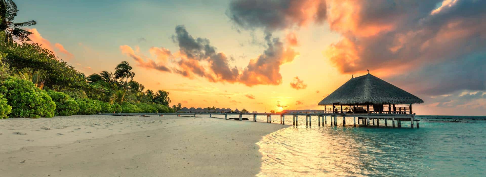 Tropical beach at sunset with overwater bungalow, palm trees, and vibrant sky, perfect for luxury travel